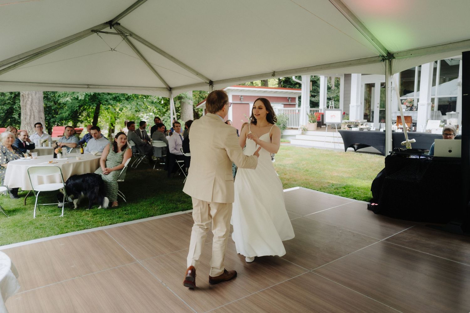 Couple shares their first dance under a white tent at an outdoor wedding reception.