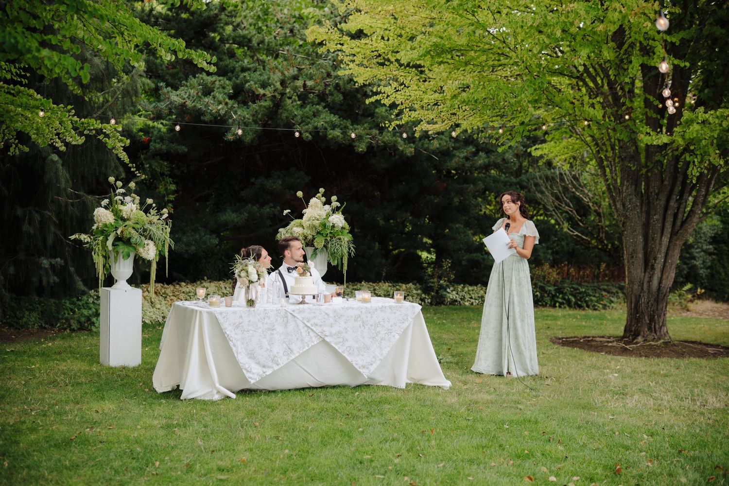 Outdoor wedding reception space with white tables and natural greenery backdrop.