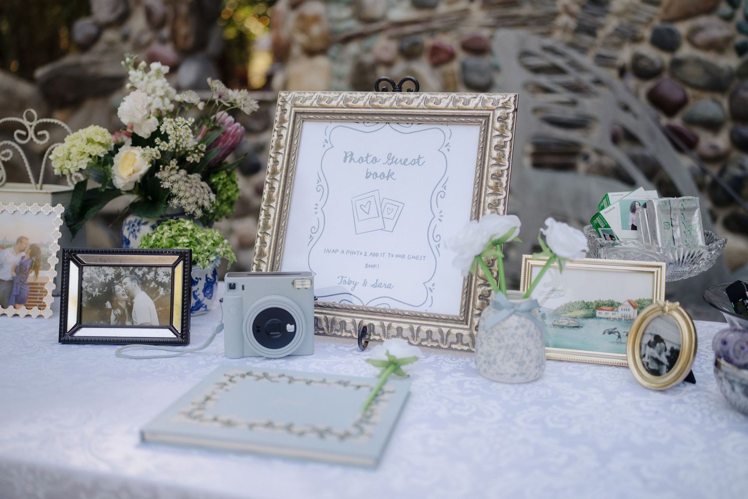 Elegant wedding reception table display with framed artwork, floral arrangements and decorative items on white linen.