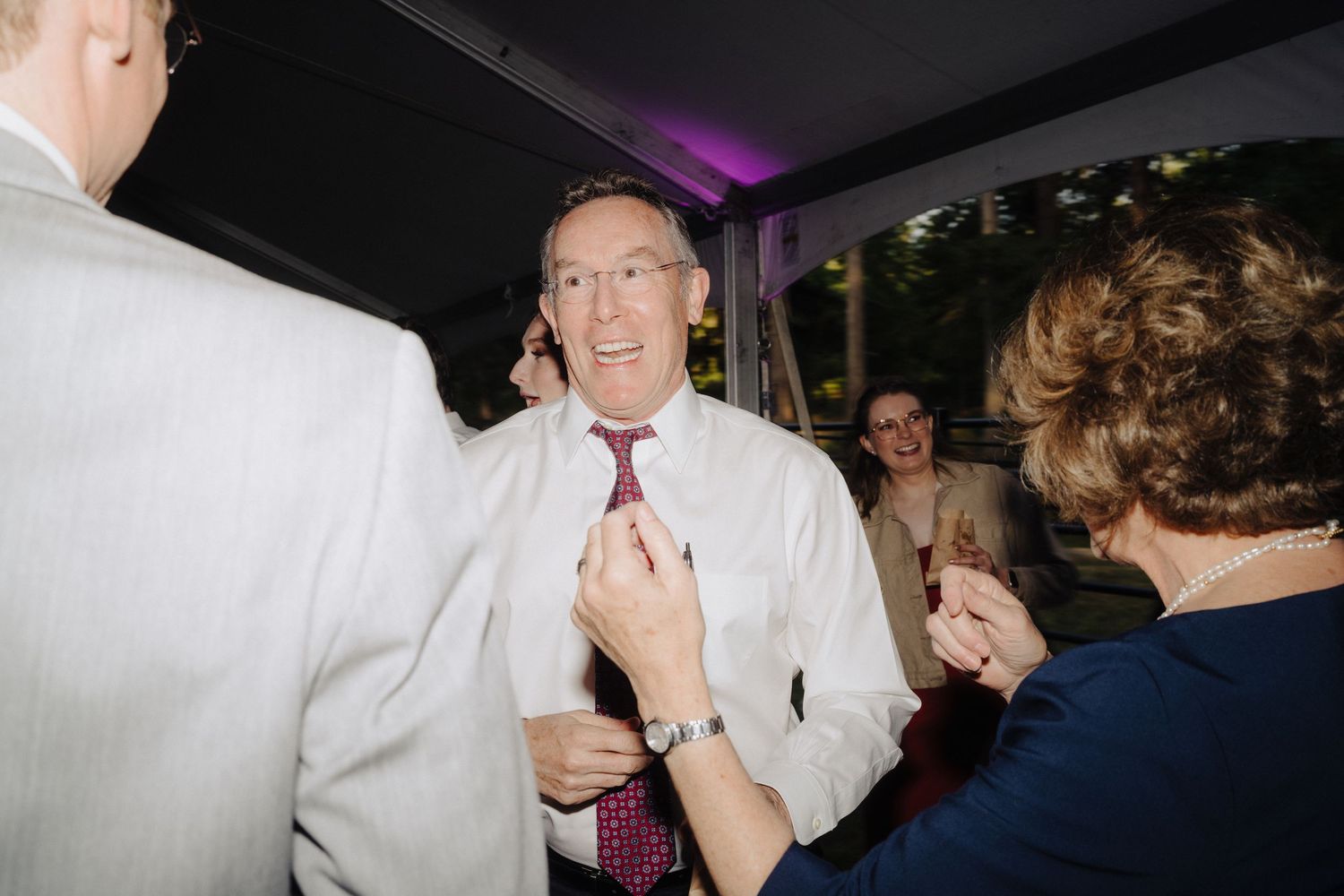 Wedding reception guests dance and celebrate under a white tent with party lighting.