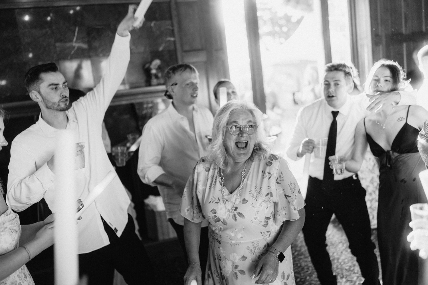 Wedding reception party guests dancing and celebrating in a dimly lit venue.