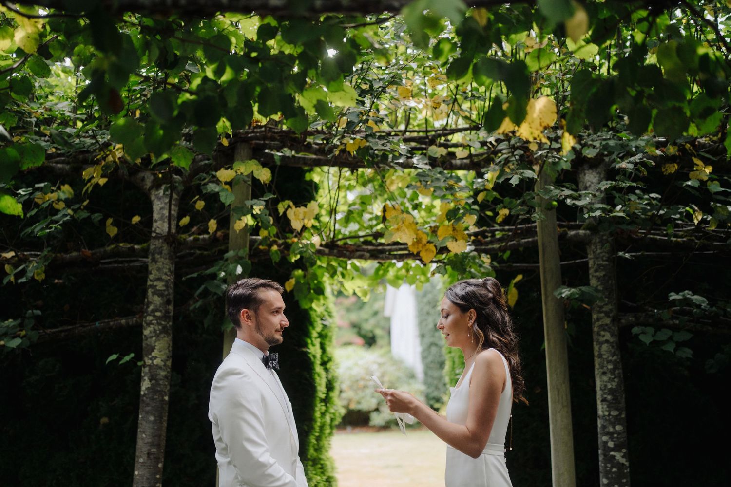 Outdoor wedding ceremony setup with white chairs and natural greenery in a garden setting.