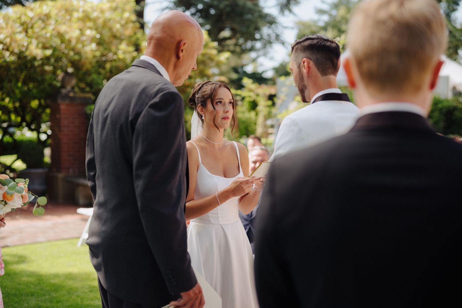 A couple in wedding attire shares a tender moment during their outdoor garden ceremony.