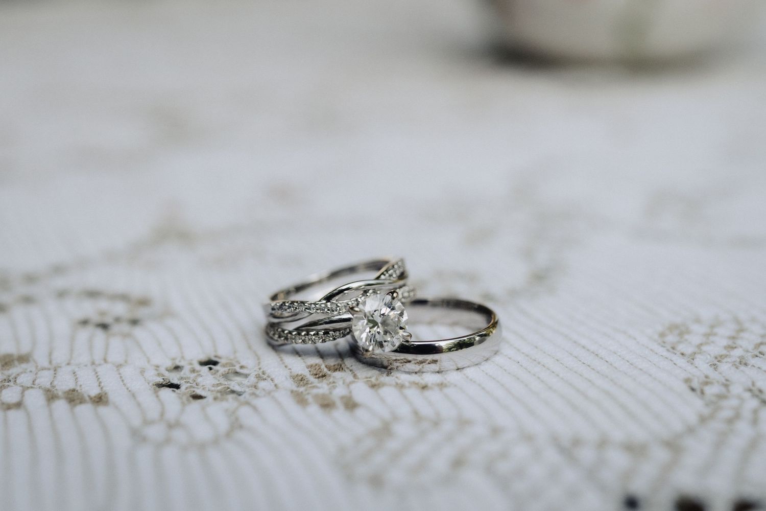 Elegant diamond engagement ring and wedding band photographed on white lace fabric.