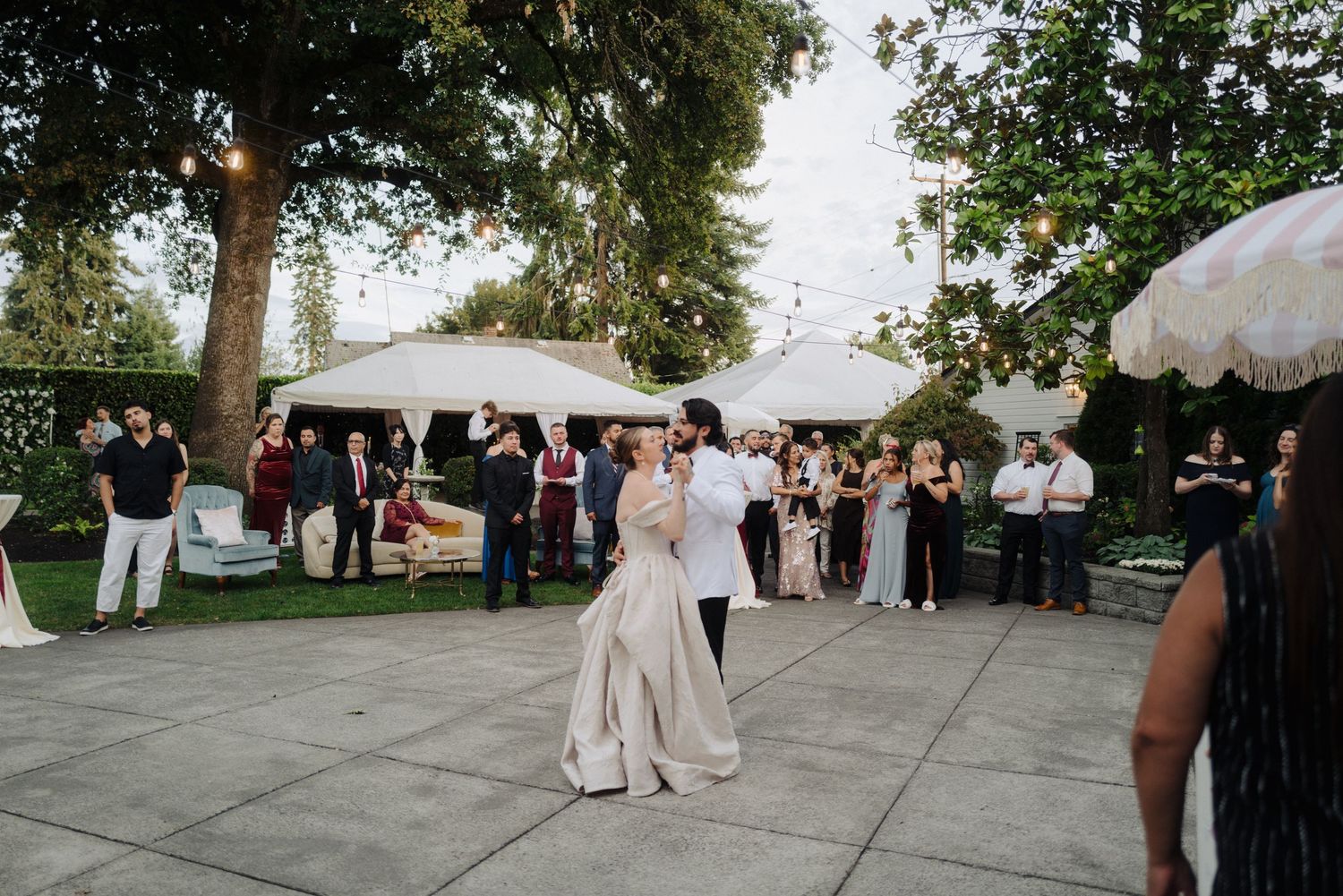 Wedding celebration on a spacious stone patio surrounded by lush trees and white tents.