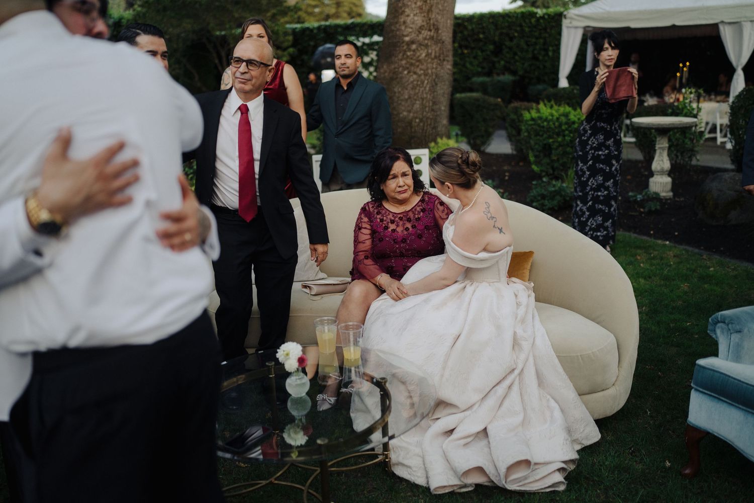 Wedding reception scene with guests mingling and a bride seated on an elegant cream-colored sofa.
