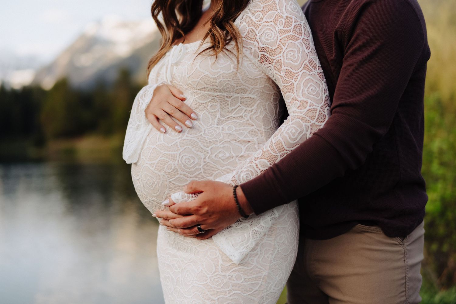 Maternity photo session with couple embracing by scenic mountain lake.