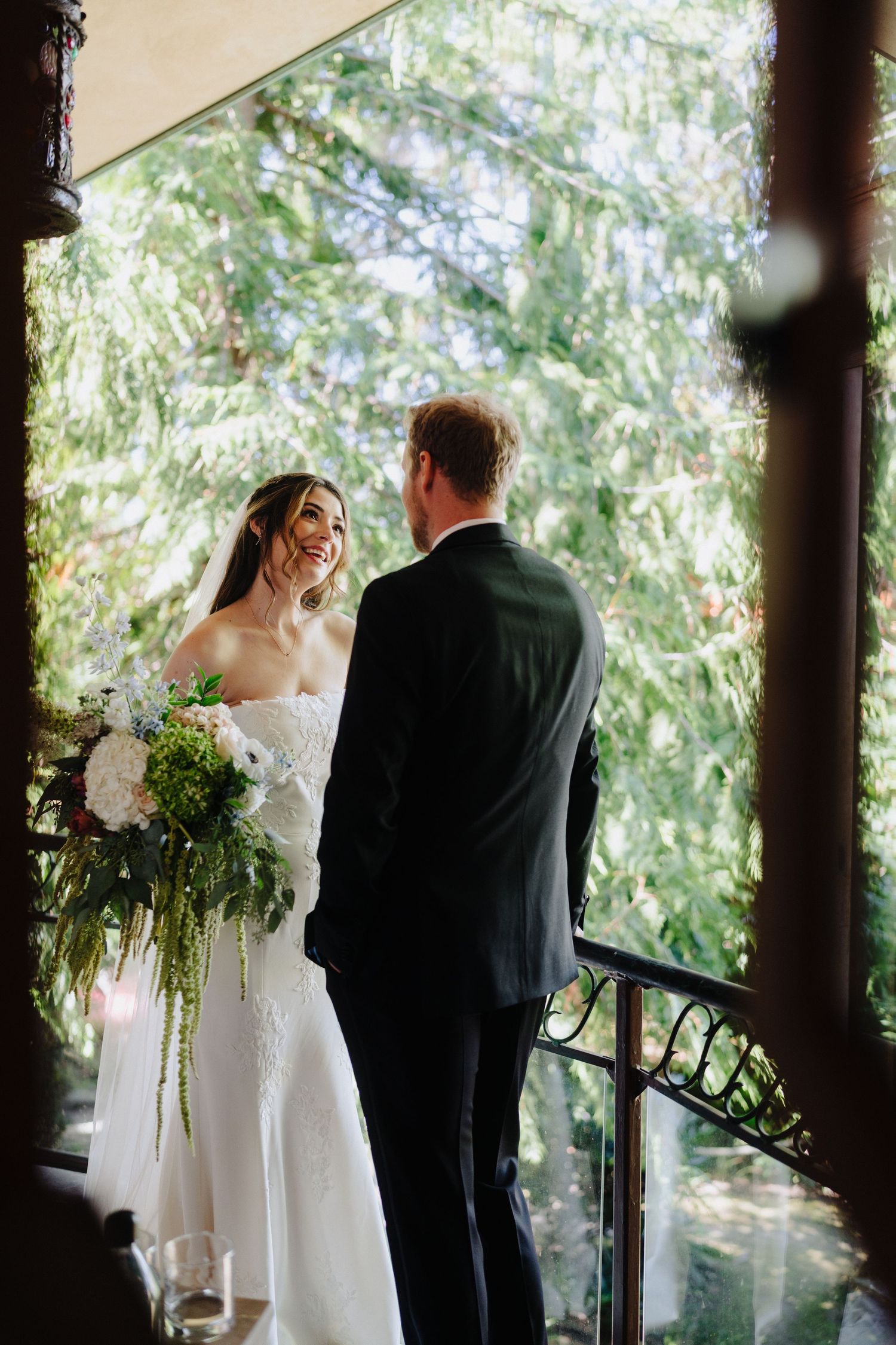 Wedding couple shares a private moment under a covered porch surrounded by evergreen trees.