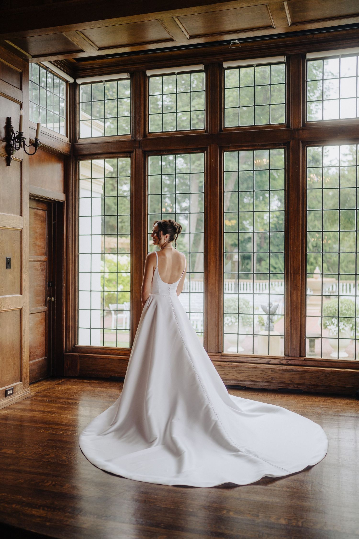 Elegant white wedding dress with dramatic train displayed in sunlit room with hardwood floors and large windows.
