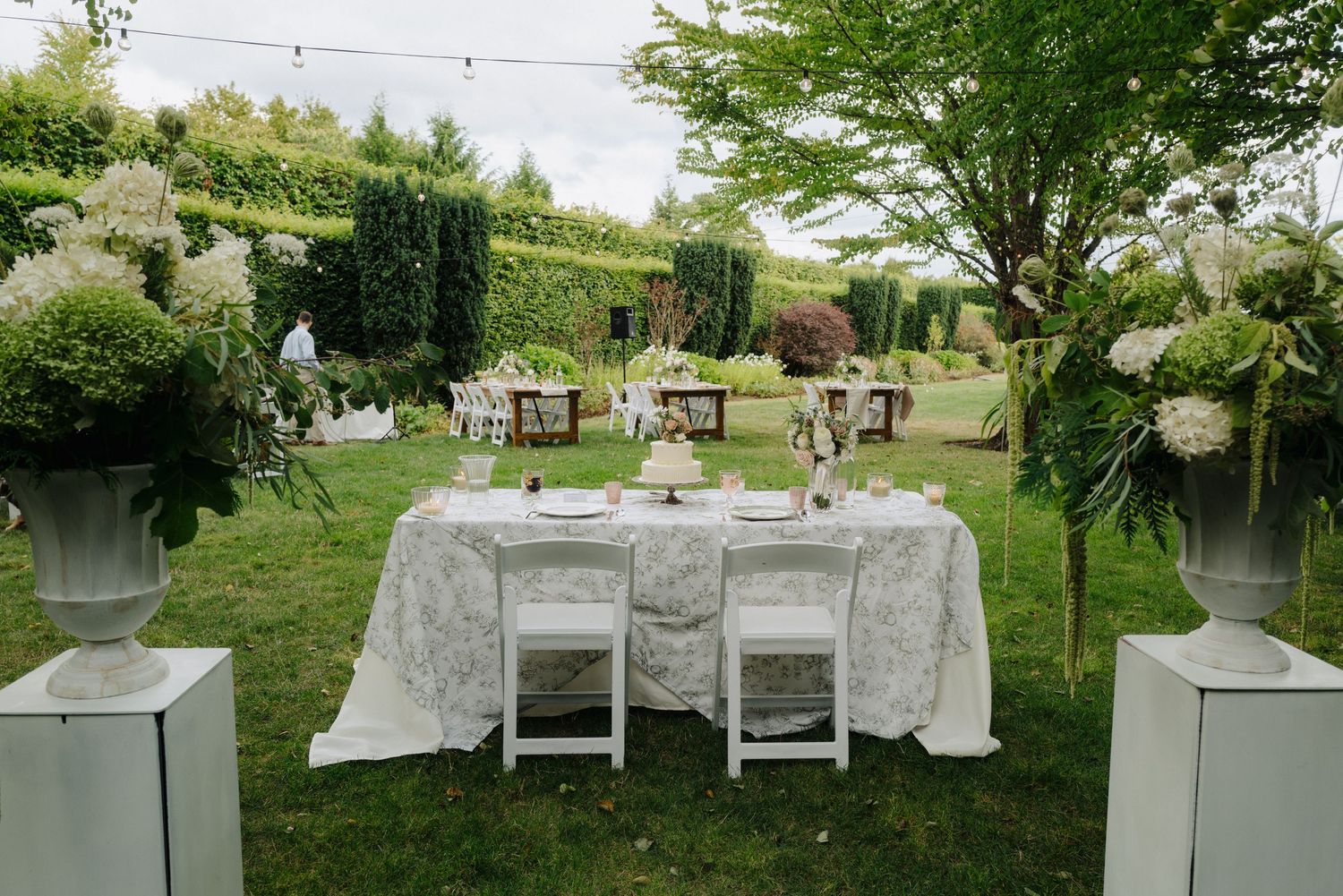 Elegant outdoor wedding reception setup with white furniture and string lights.