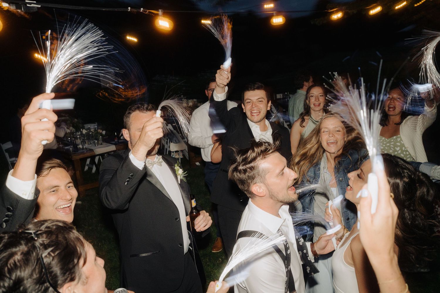 Wedding celebration at night with guests dancing and celebrating under ambient lighting.