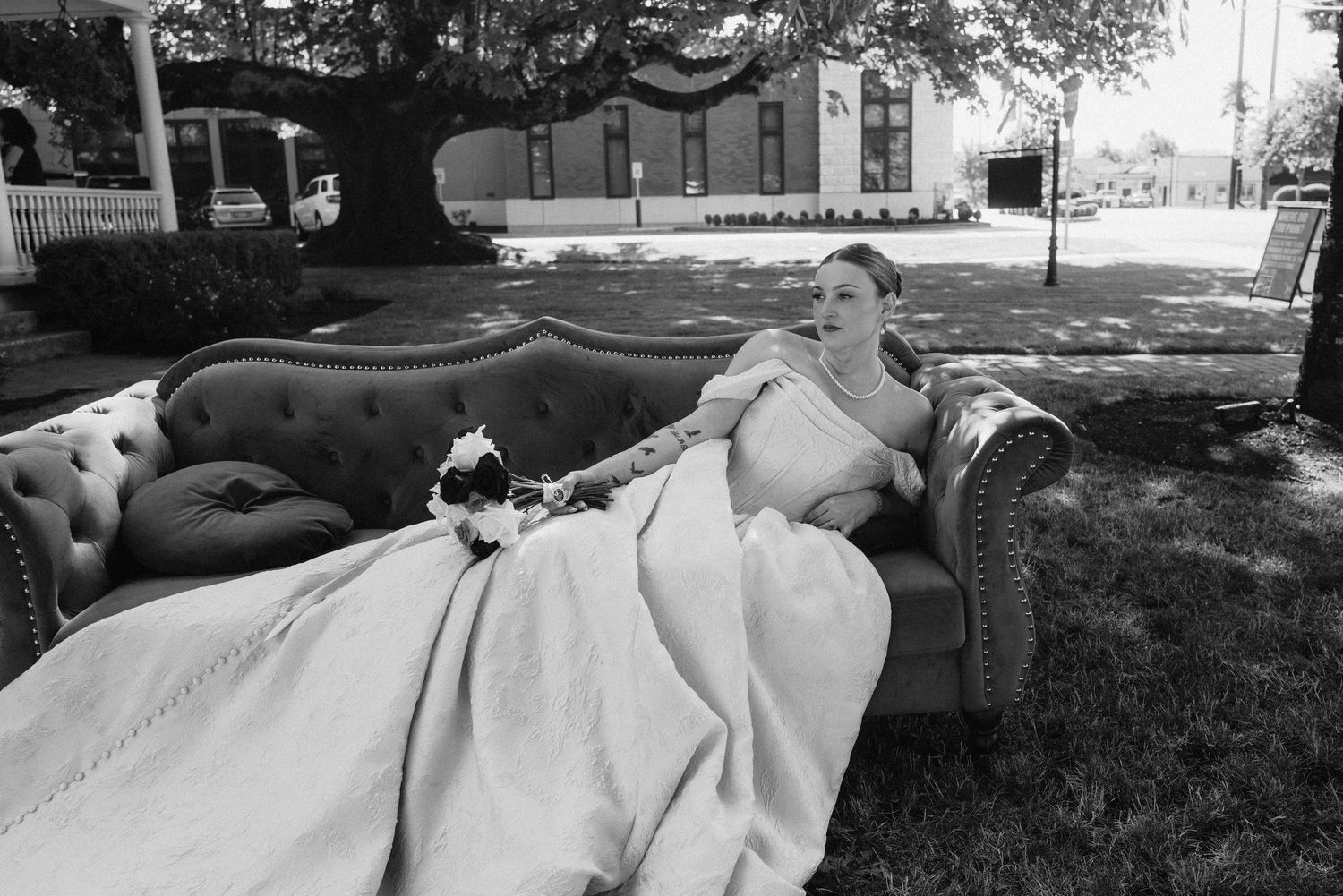 Flowing white wedding dress train spreads across green grass during outdoor photography session.