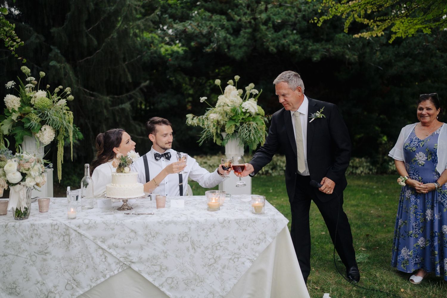 Wedding guests gathered around a white-clothed table during an outdoor garden reception.