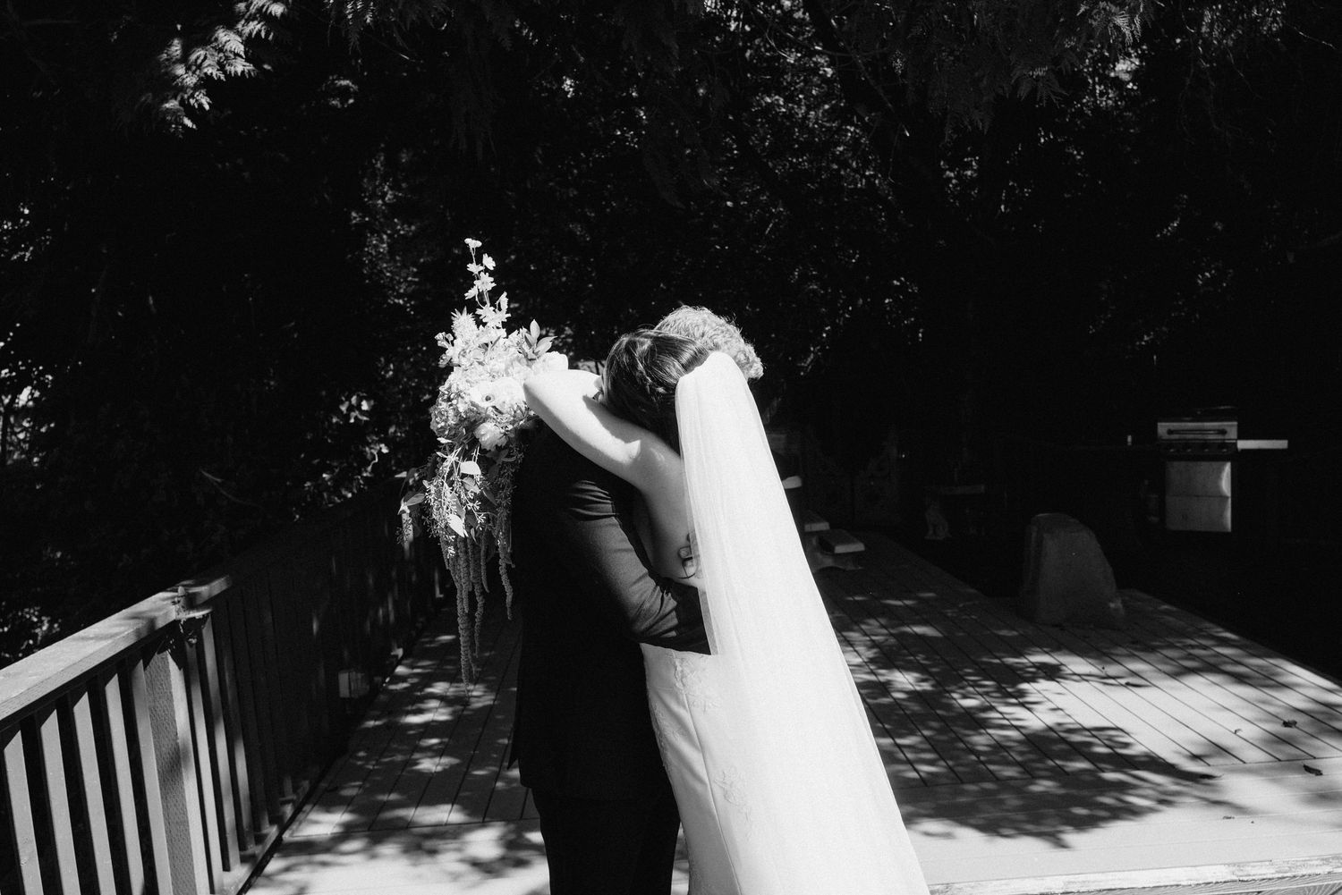 A bride and groom share an intimate moment together in a garden setting with dappled sunlight and shadows.