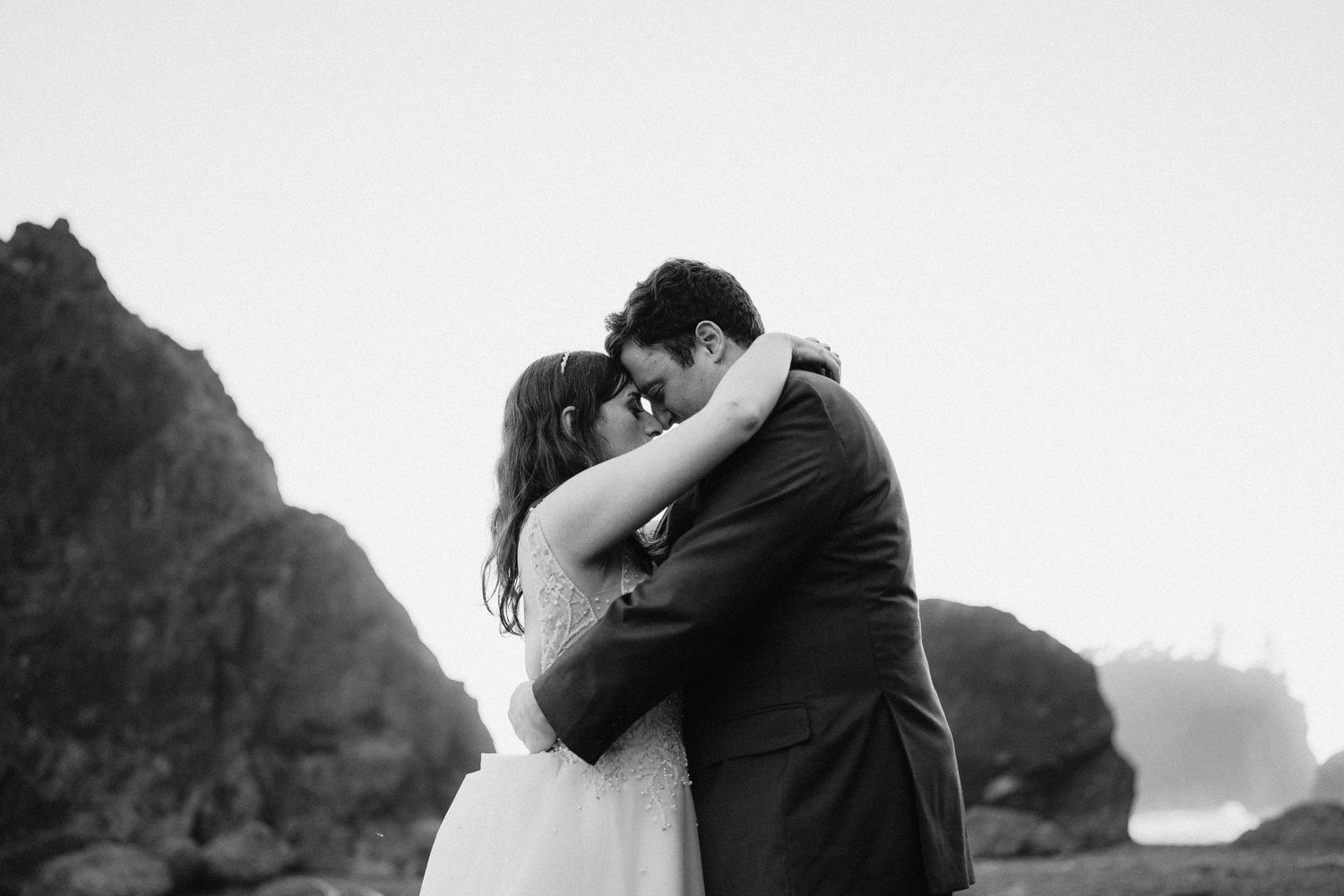 Romantic black and white wedding portrait with dramatic coastal cliffs in background.
