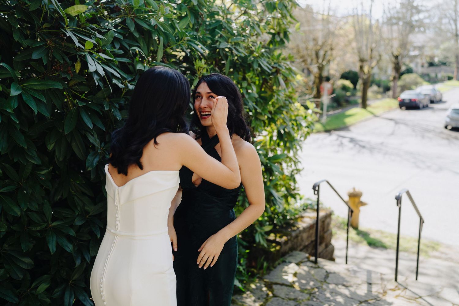 Two people share a joyful moment outdoors near green foliage.