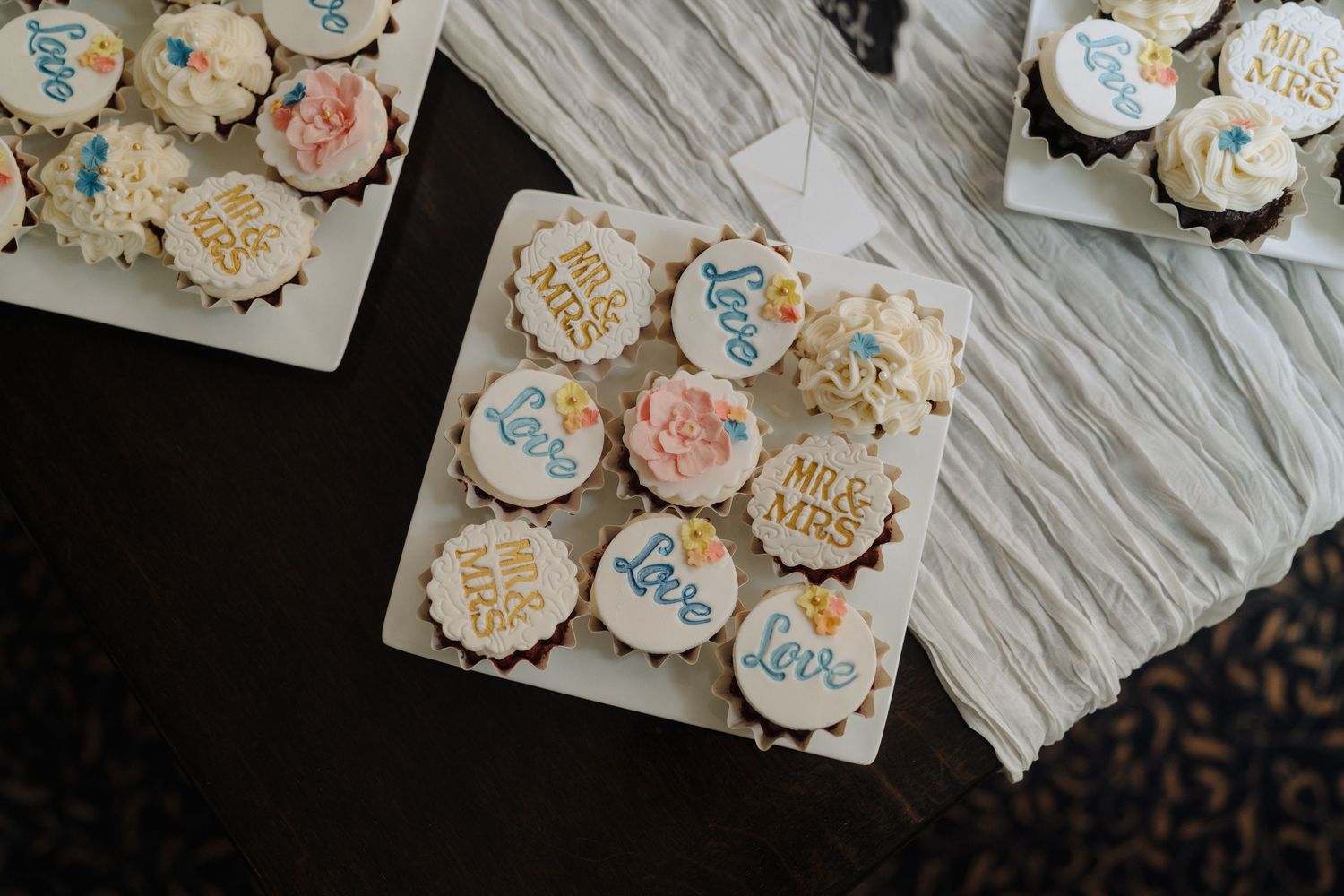 Decorative wedding cupcakes with blue and pink frosting arranged on white plates.