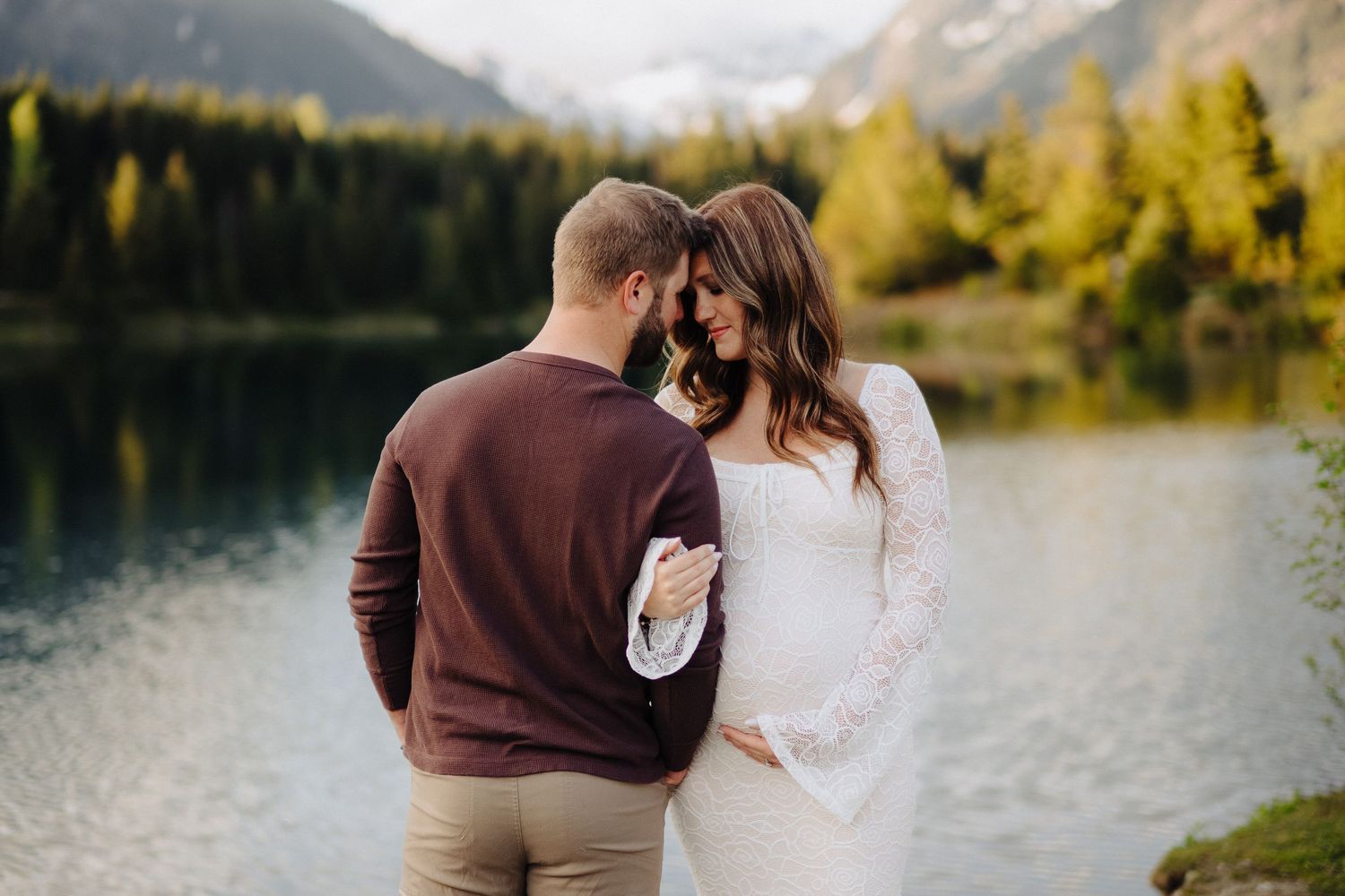 An intimate embrace captured during a lakeside maternity session with mountain views.