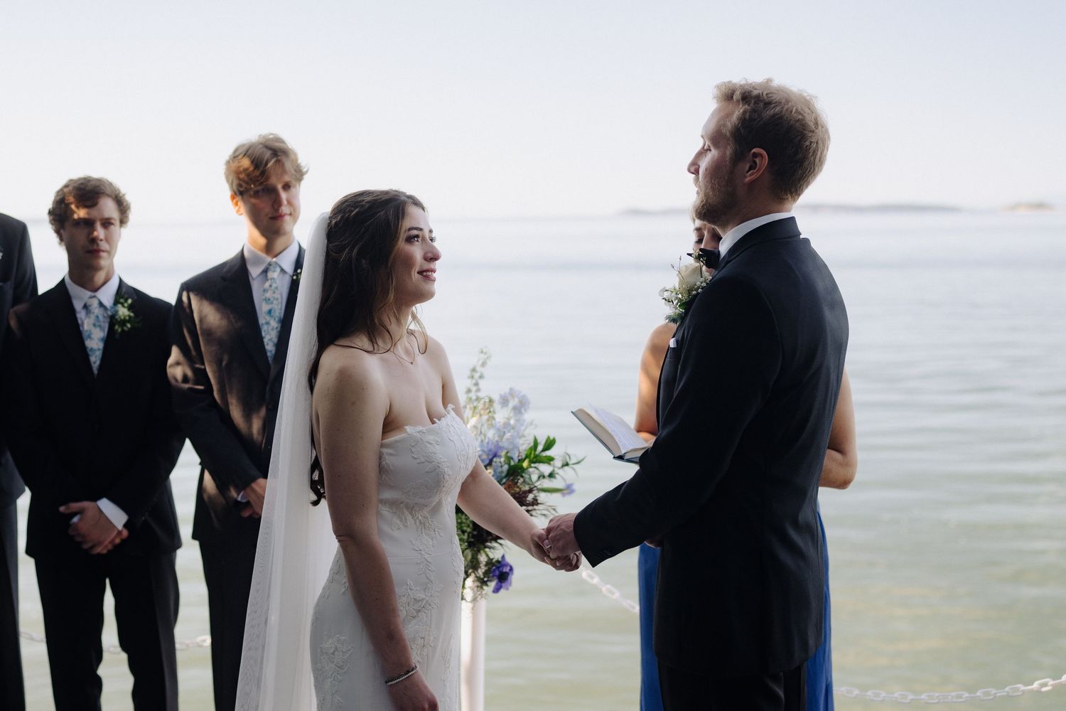 Wedding ceremony in progress with attendees gathered by the waterfront on a clear day.