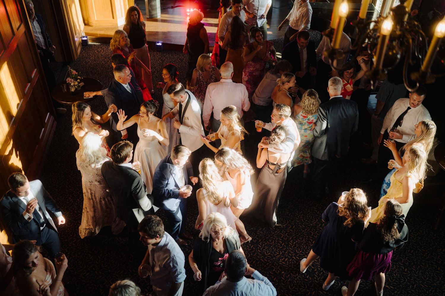 Overhead view of a crowded wedding reception dance floor with guests dancing under warm lighting.