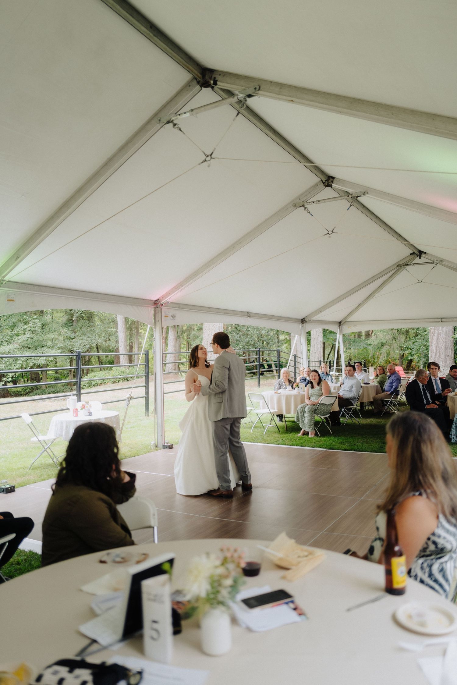 A white wedding reception tent set up outdoors with tables and chairs arranged for guests under the canopy.
