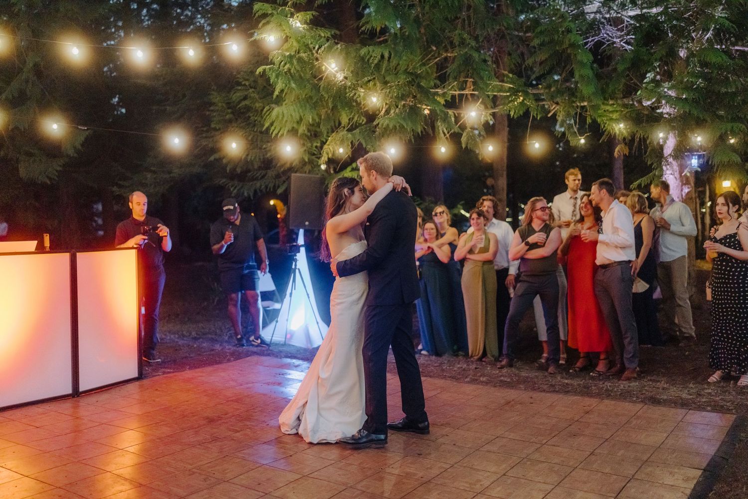 Evening outdoor wedding reception with string lights illuminating guests dancing on a patio.