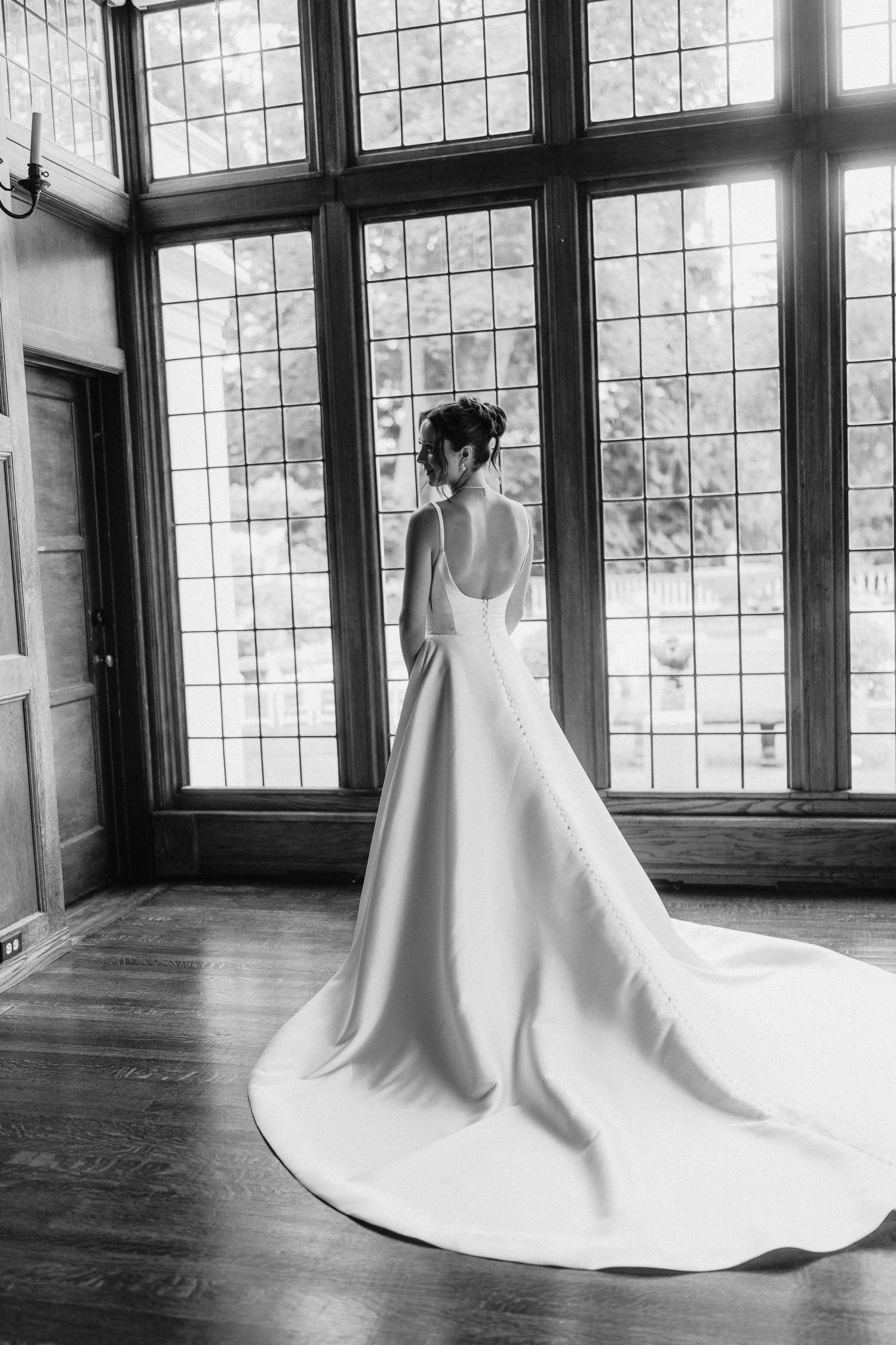A wedding dress with a dramatic train is showcased in a room with elegant leaded glass windows.