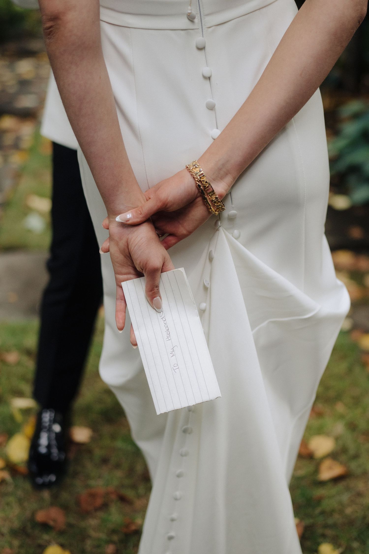 Close-up of hands holding a small white paper or note card during an outdoor wedding ceremony.