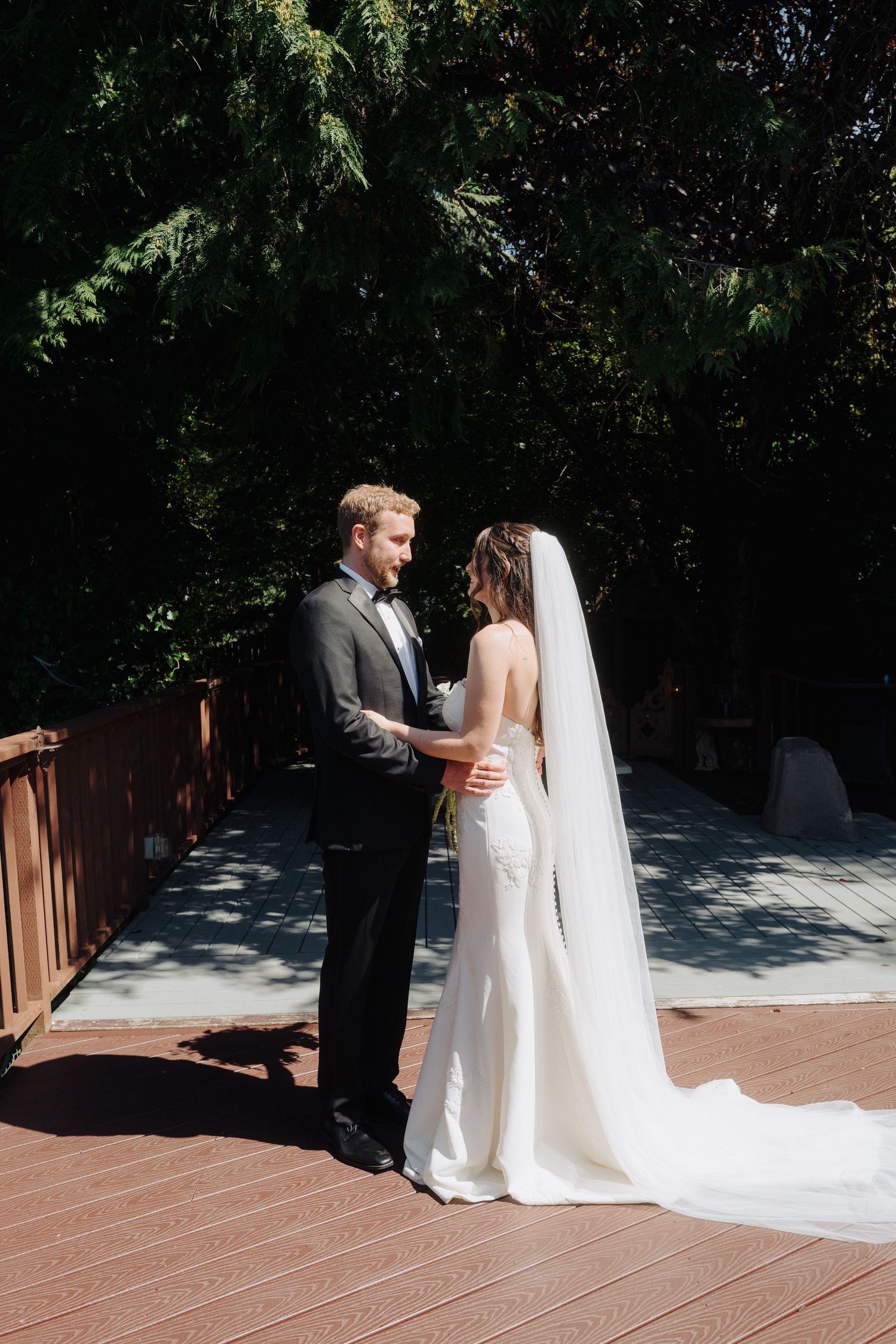 A couple shares an intimate moment on a wooden deck surrounded by trees on their wedding day.