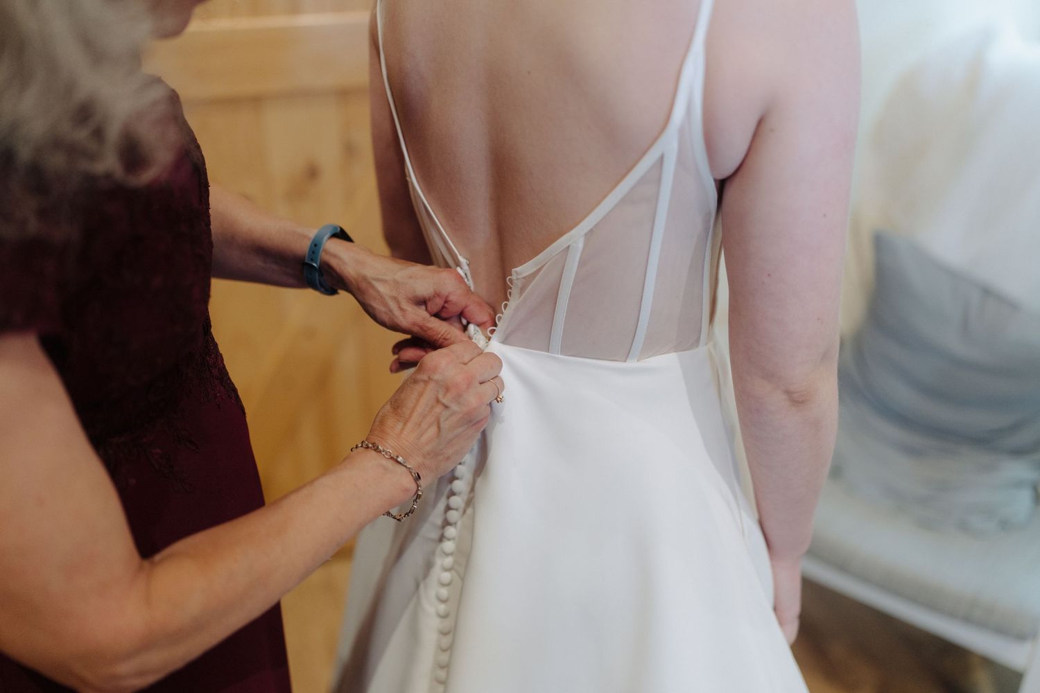 Close-up view of someone fastening delicate buttons on the back of an elegant white wedding dress.