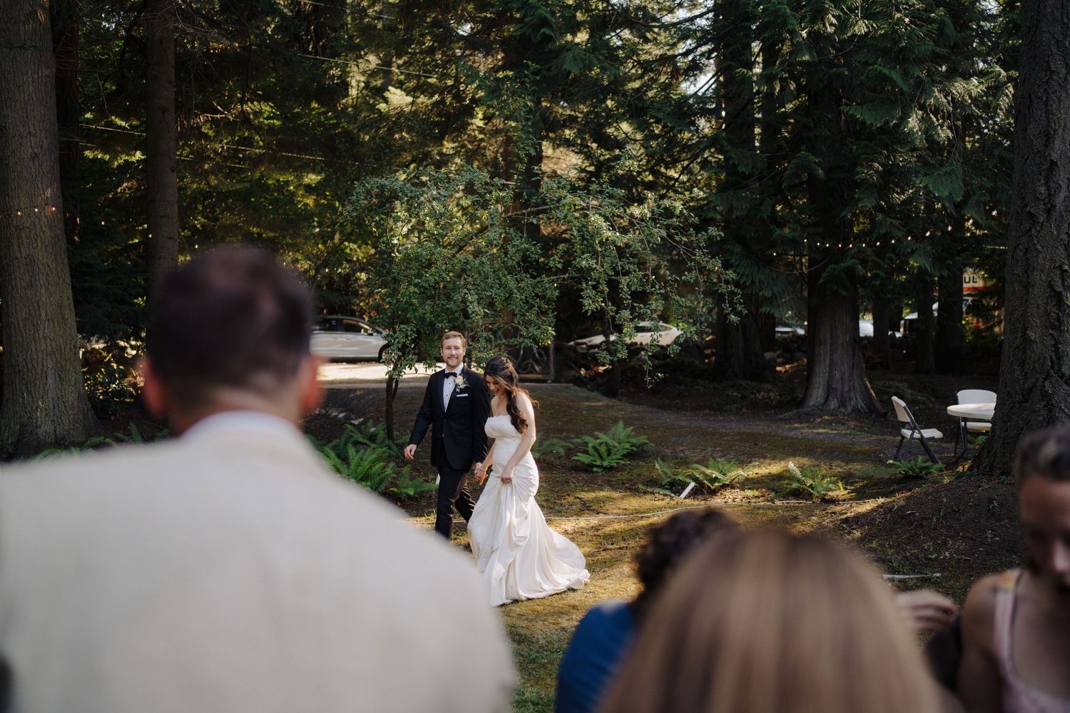 Wedding couple photographed from a distance in a wooded outdoor setting.