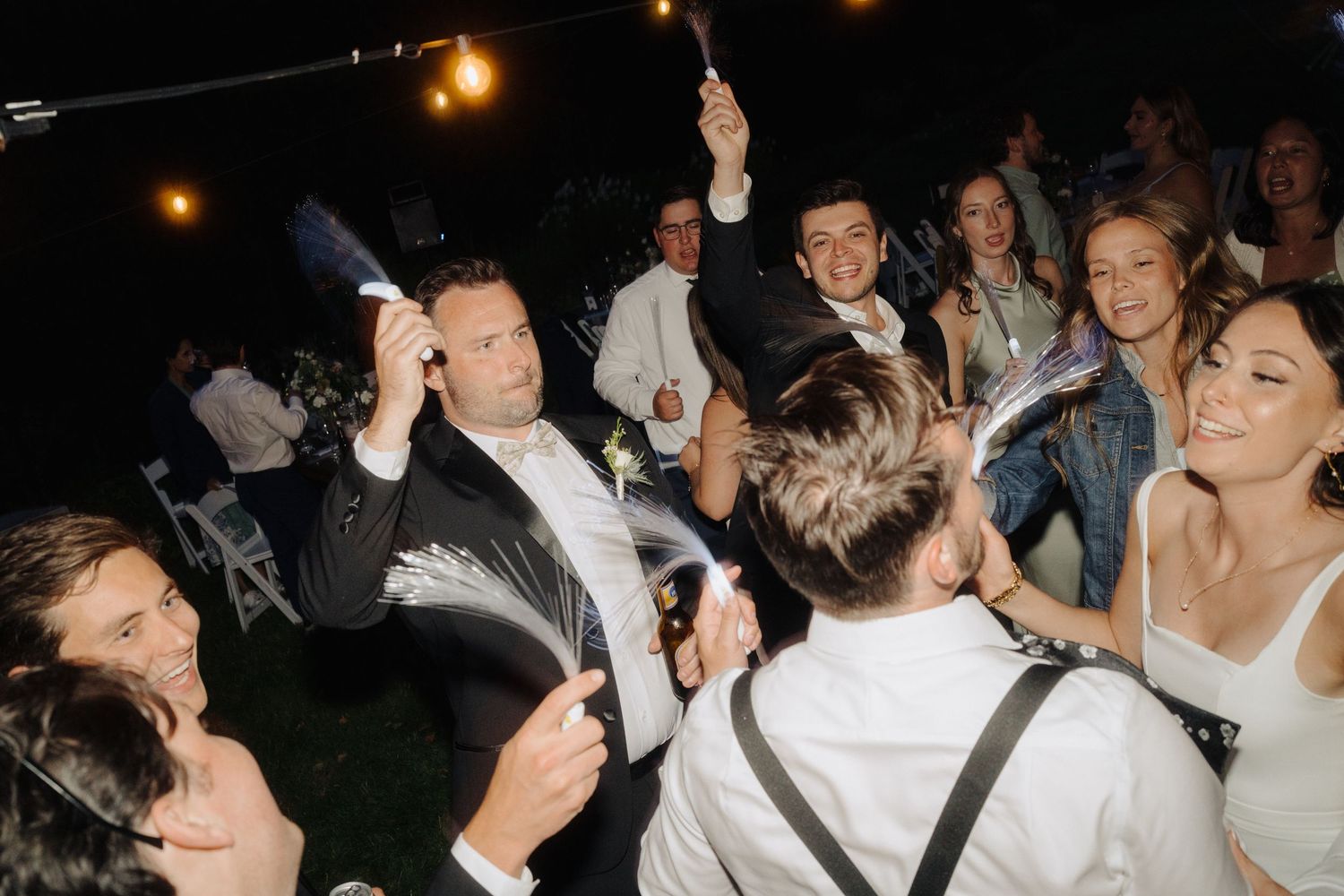 A lively nighttime wedding reception with guests dancing and celebrating under string lights.