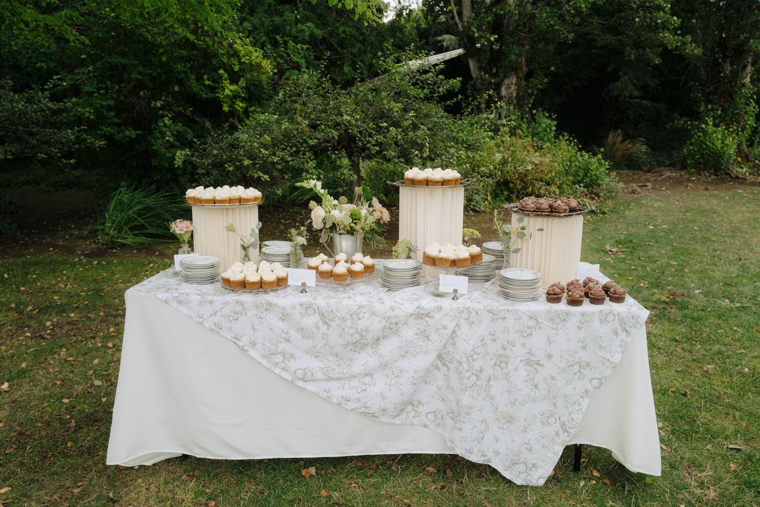 Long white-clothed tables display desserts and treats at an outdoor wedding reception.