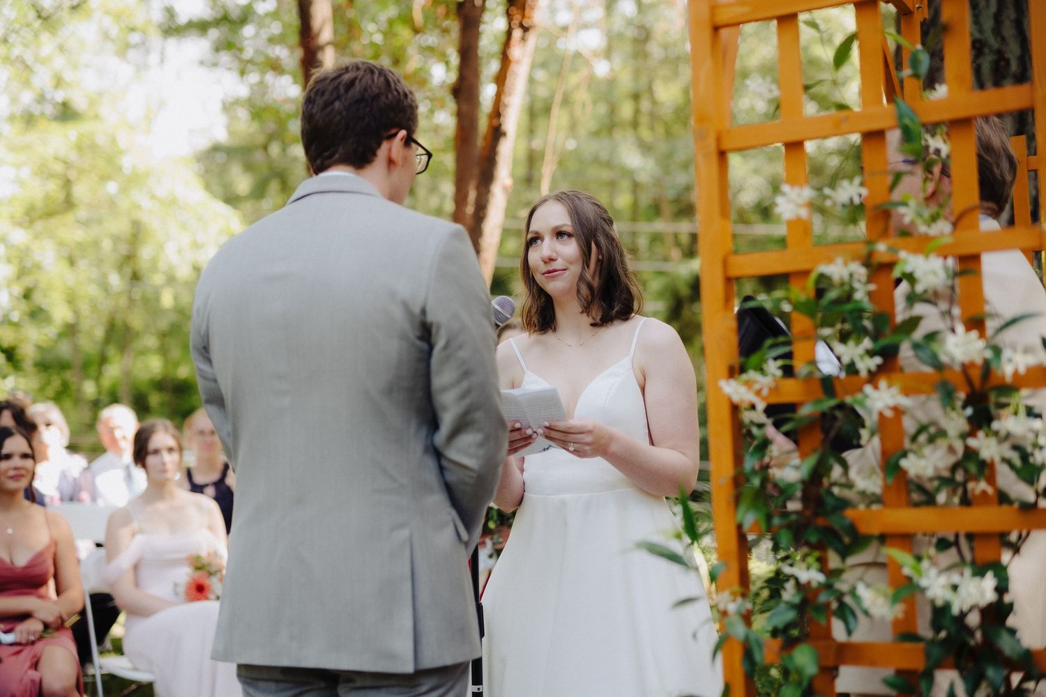Outdoor wedding ceremony setup with wooden arbor decorated with floral arrangements in a natural setting.