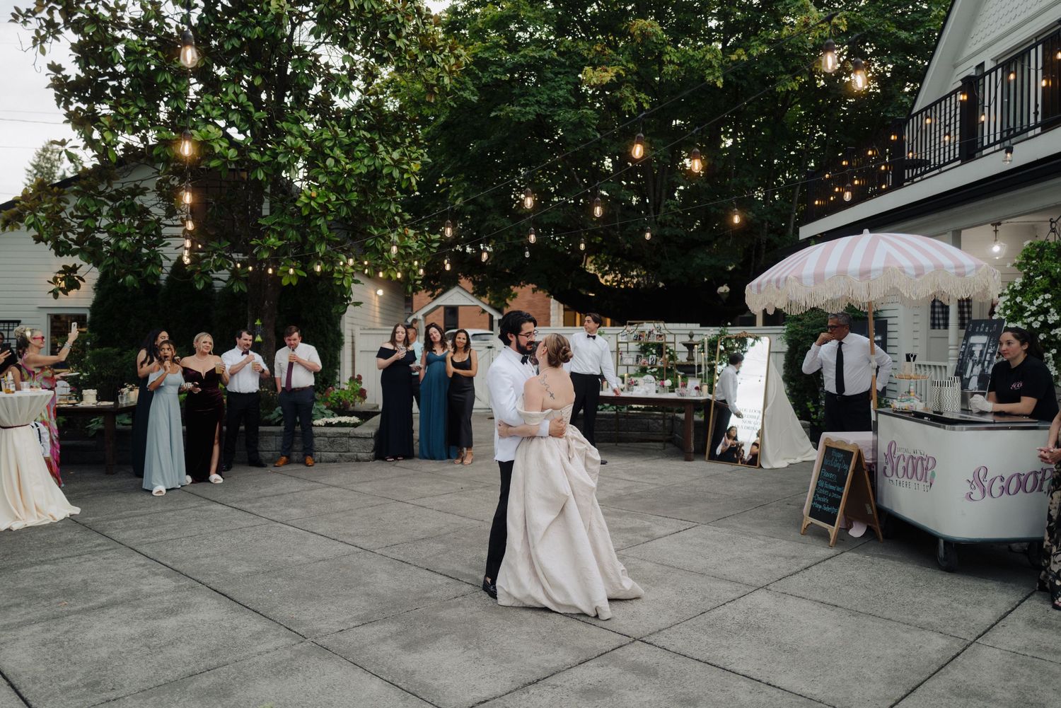 Wedding guests gathered on an outdoor patio under string lights and trees for an evening celebration.