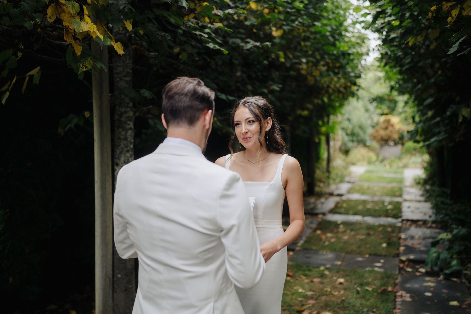 Couple sharing tender moments along a garden pathway with lush greenery overhead.
