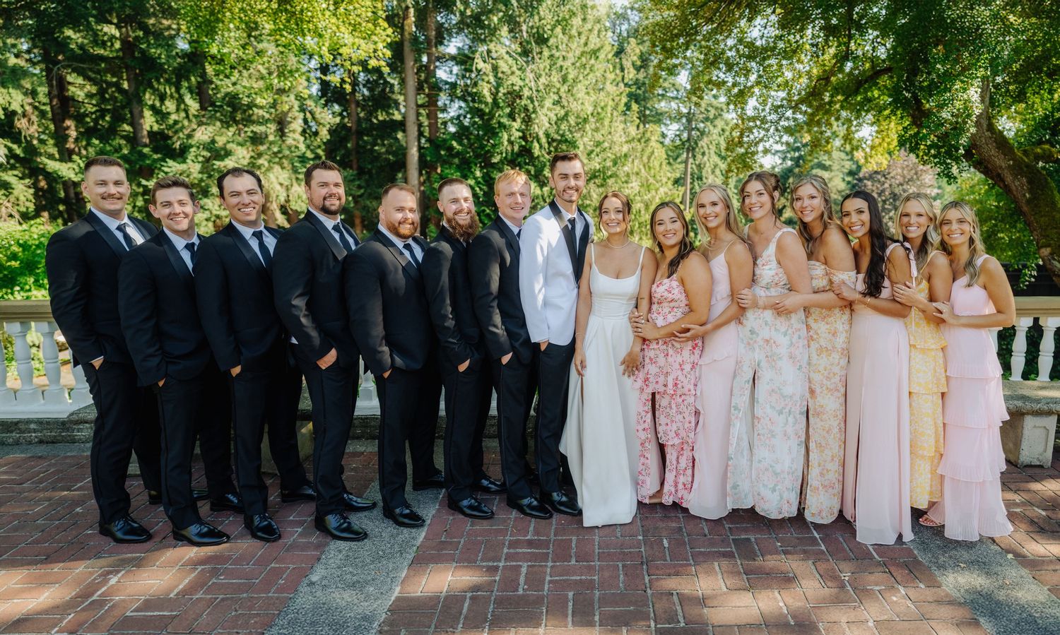 Wedding party poses outdoors in coordinated formal attire with bridesmaids in blush pink and groomsmen in dark suits.