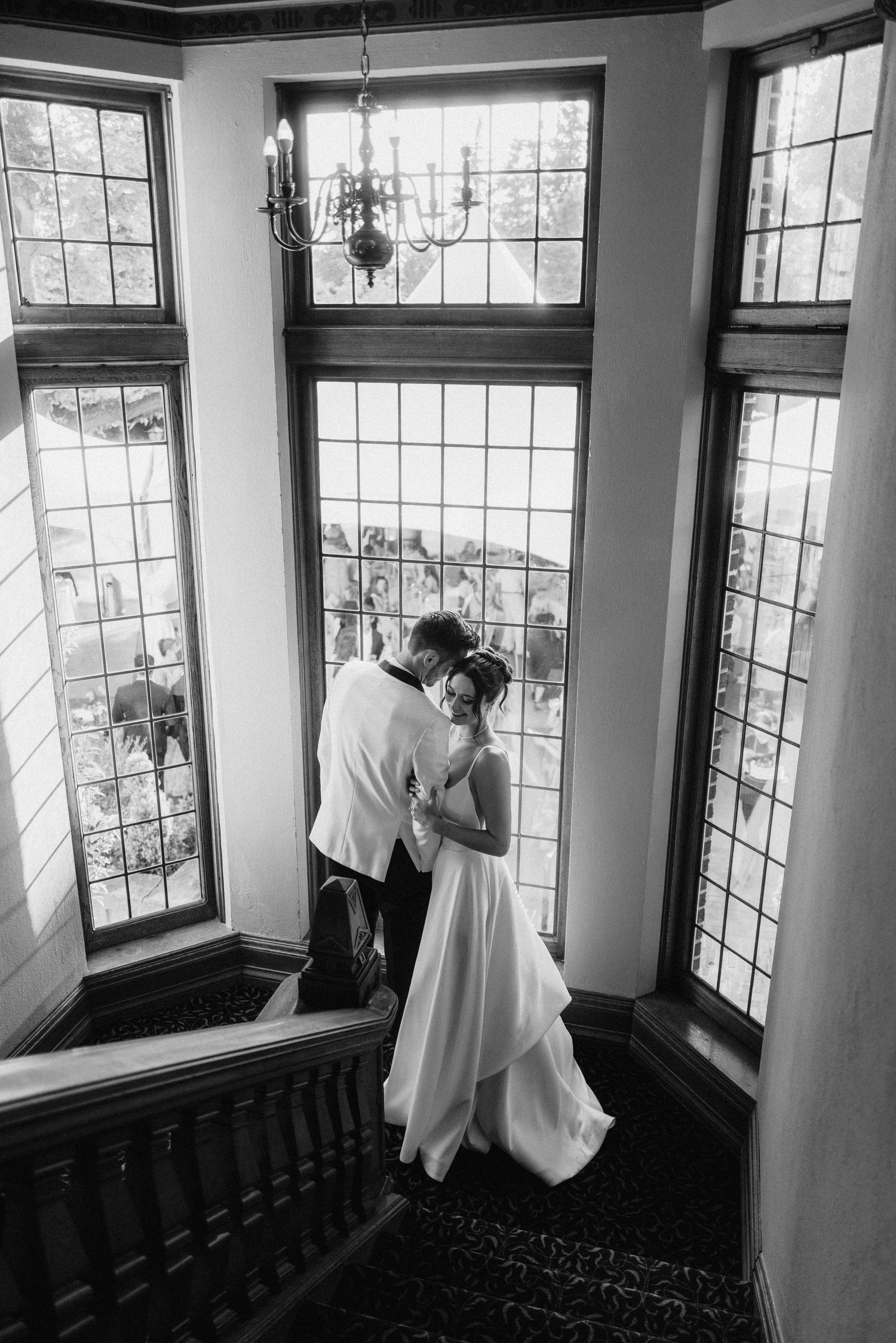 A romantic moment captured in black and white by a grand window with leaded glass details.