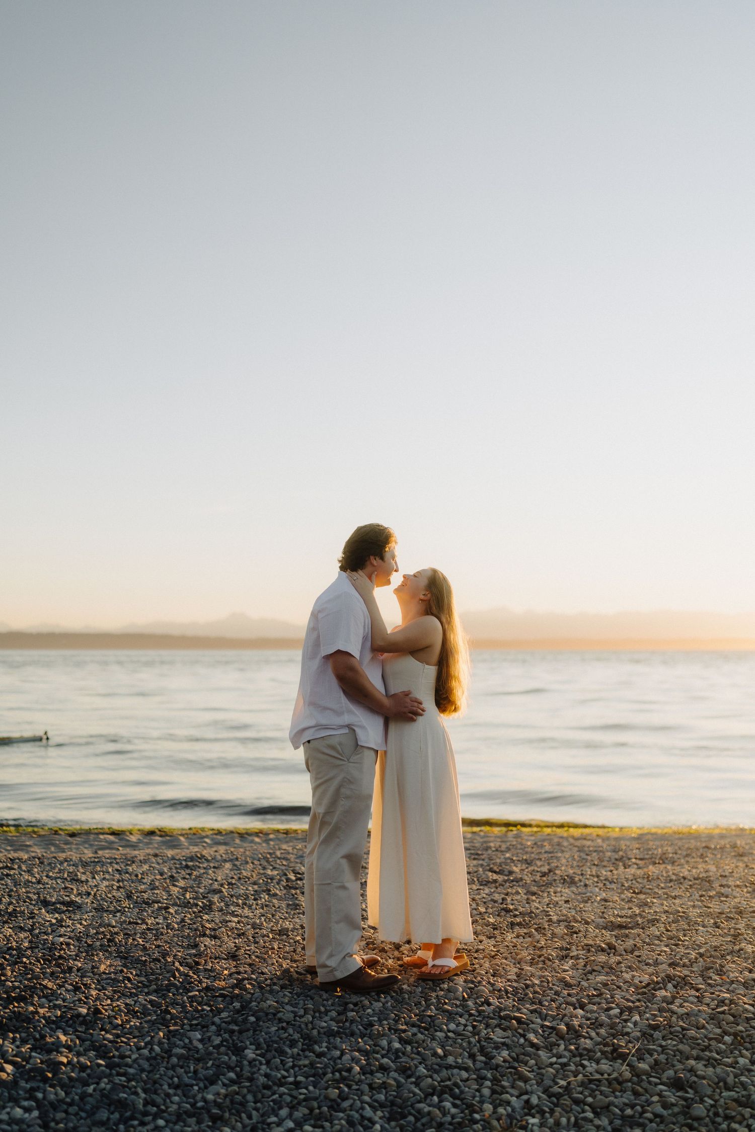 Couple shares intimate moments on a beach at sunset wearing matching white outfits.
