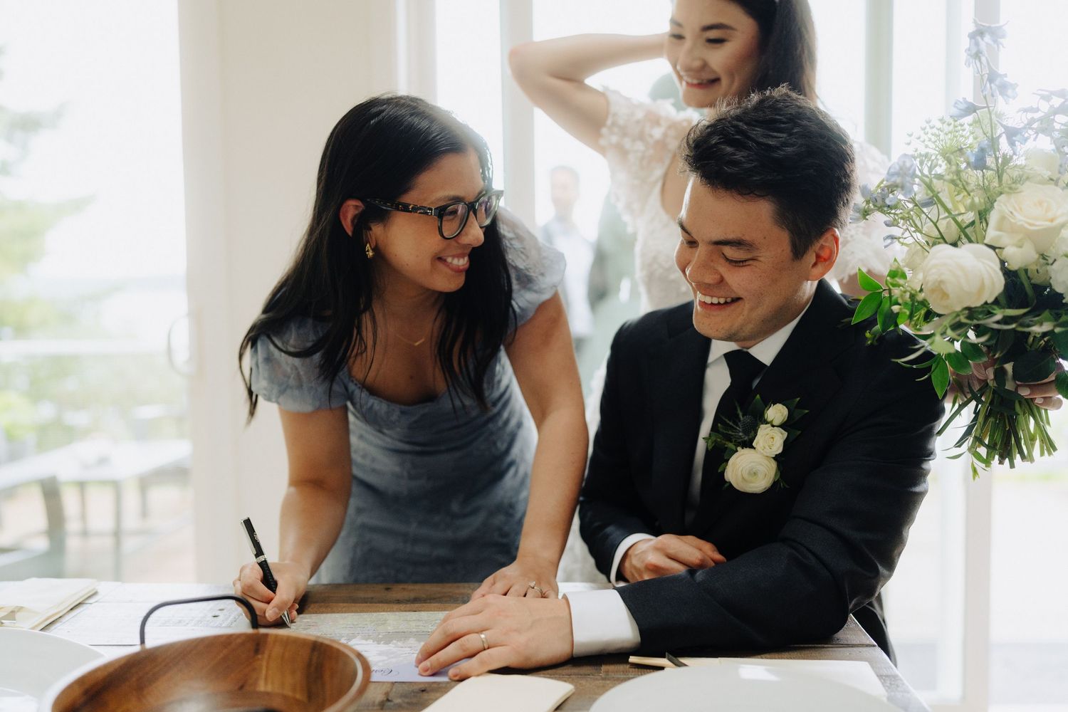 A couple shares a joyful moment while signing papers at a table decorated with white flowers.
