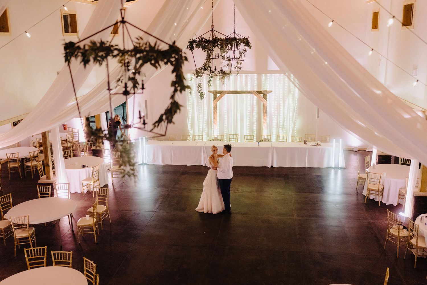 Bride and groom share first dance in beautifully draped wedding venue with floral chandeliers.