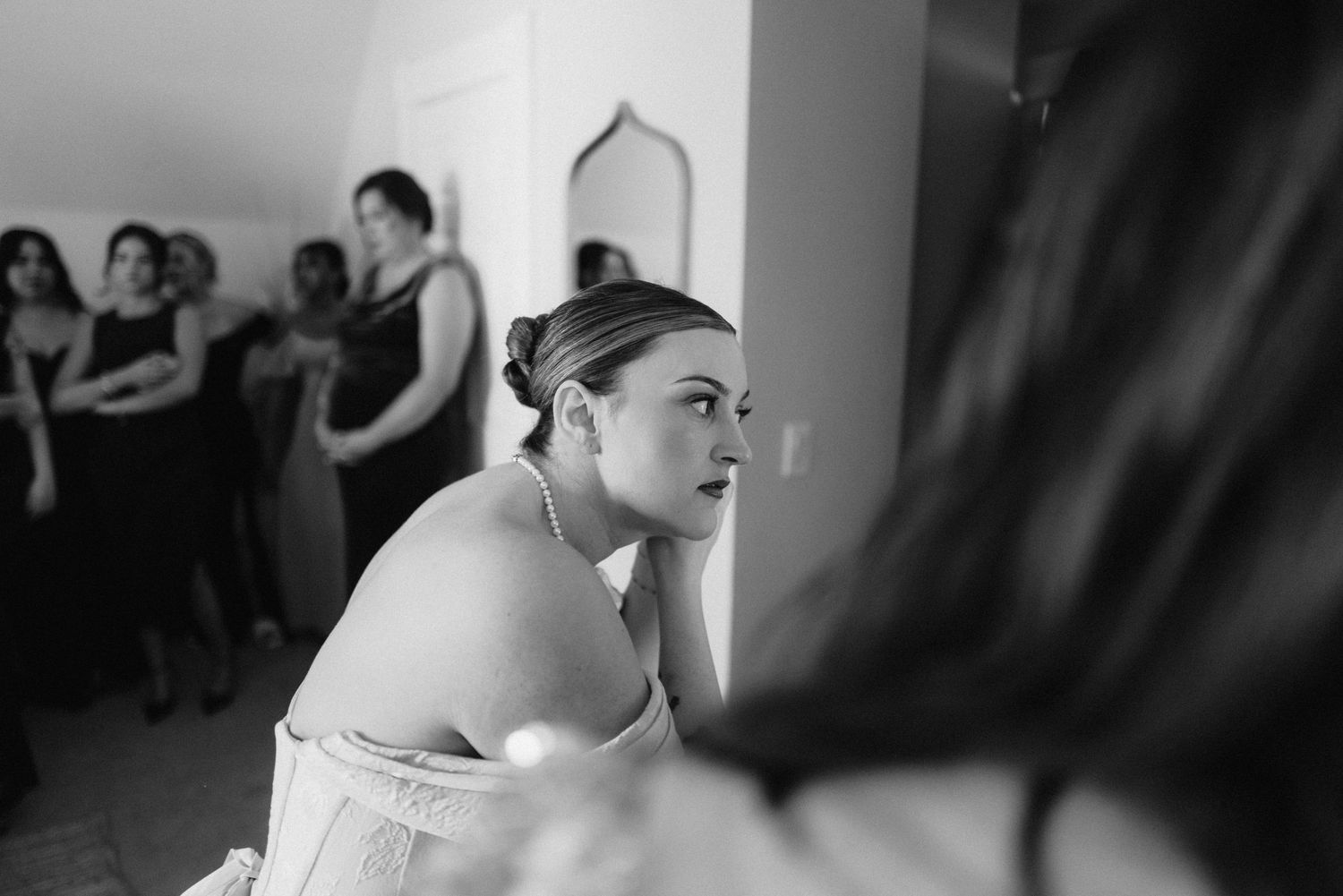 Black and white image showing preparation moments in a bridal suite with makeup application.