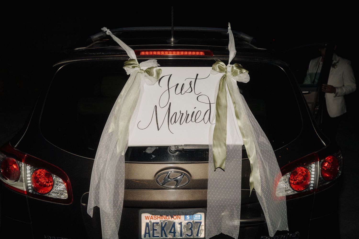 Wedding car decorated with white ribbons and 'Just Married' sign at night.