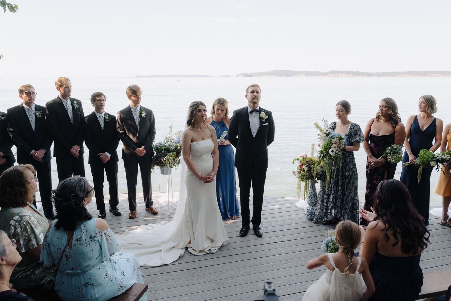 Wedding party stands in line on a scenic waterfront deck during the ceremony.