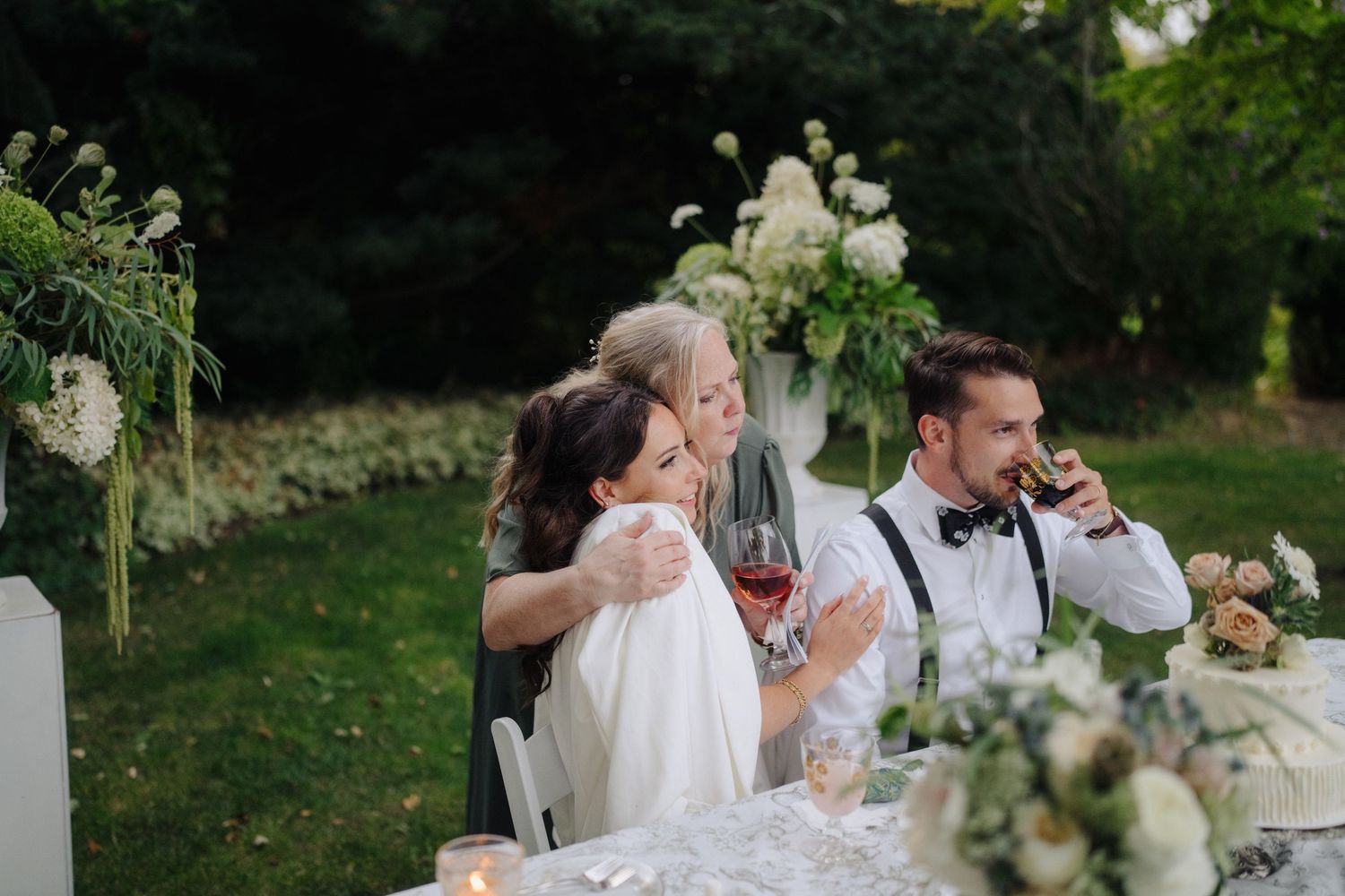 Wedding reception table setup outdoors with white linens and floral centerpieces.