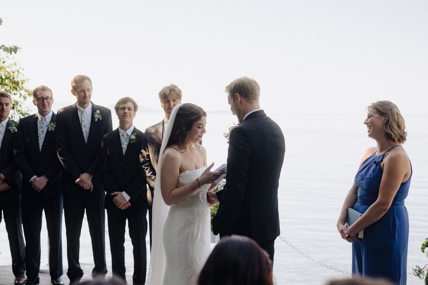 Wedding ceremony participants gathered on a bright outdoor deck by the water.