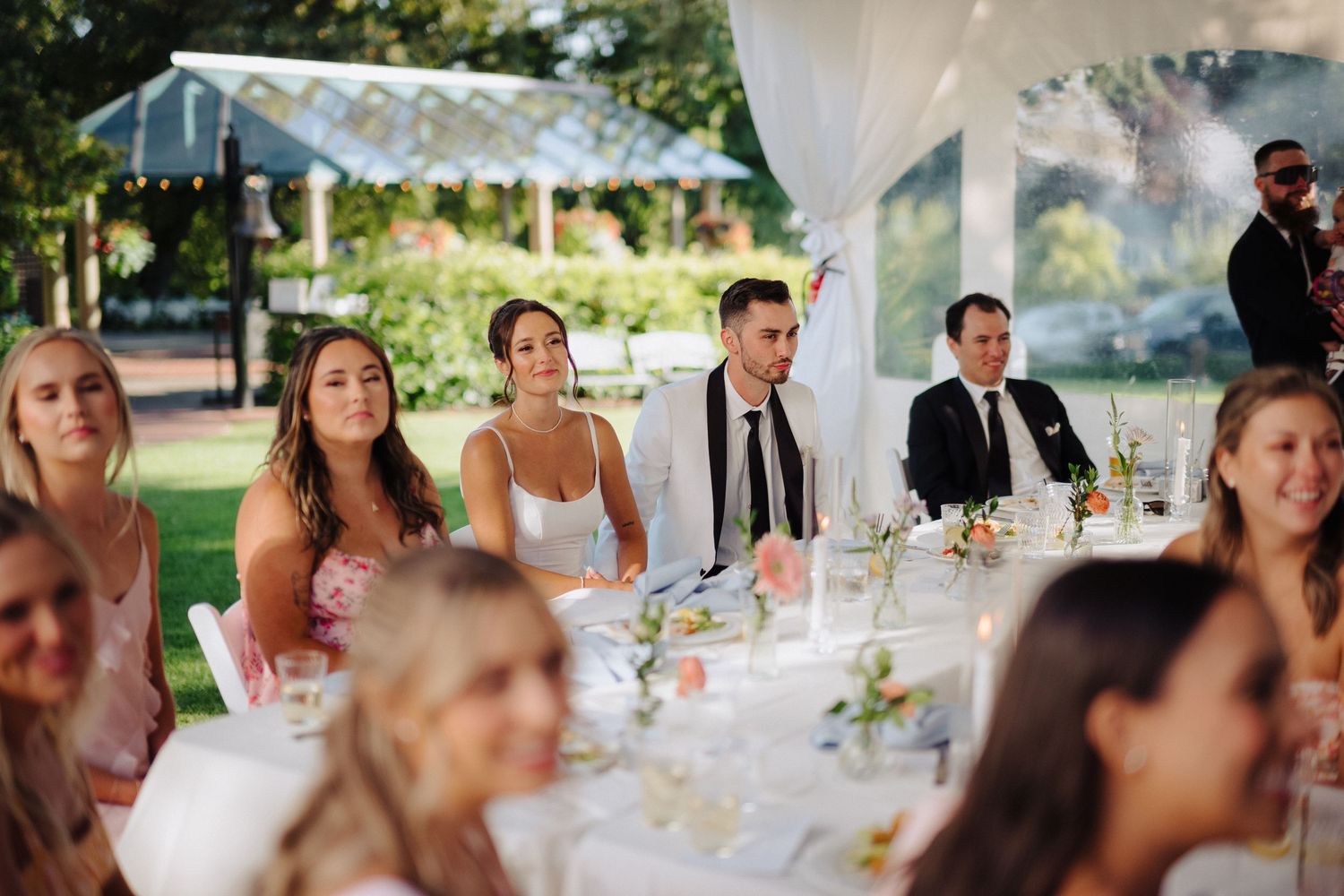 Wedding guests enjoying speeches and toasts during an outdoor tented reception.