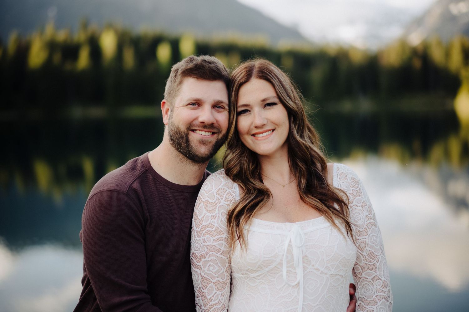 Couple sharing tender moments by a pristine mountain lake surrounded by evergreens.