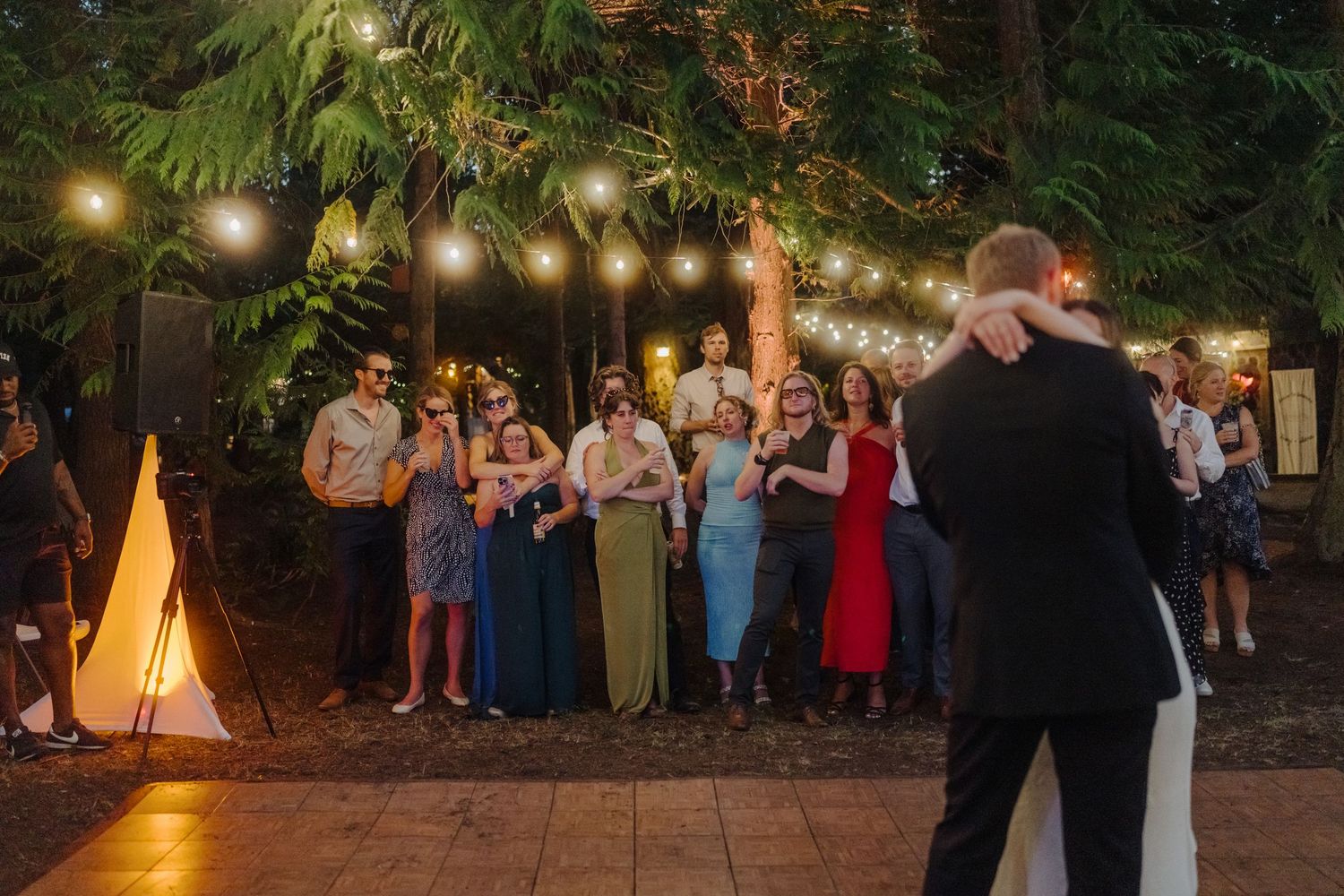 Evening wedding reception with string lights and guests dancing outdoors.