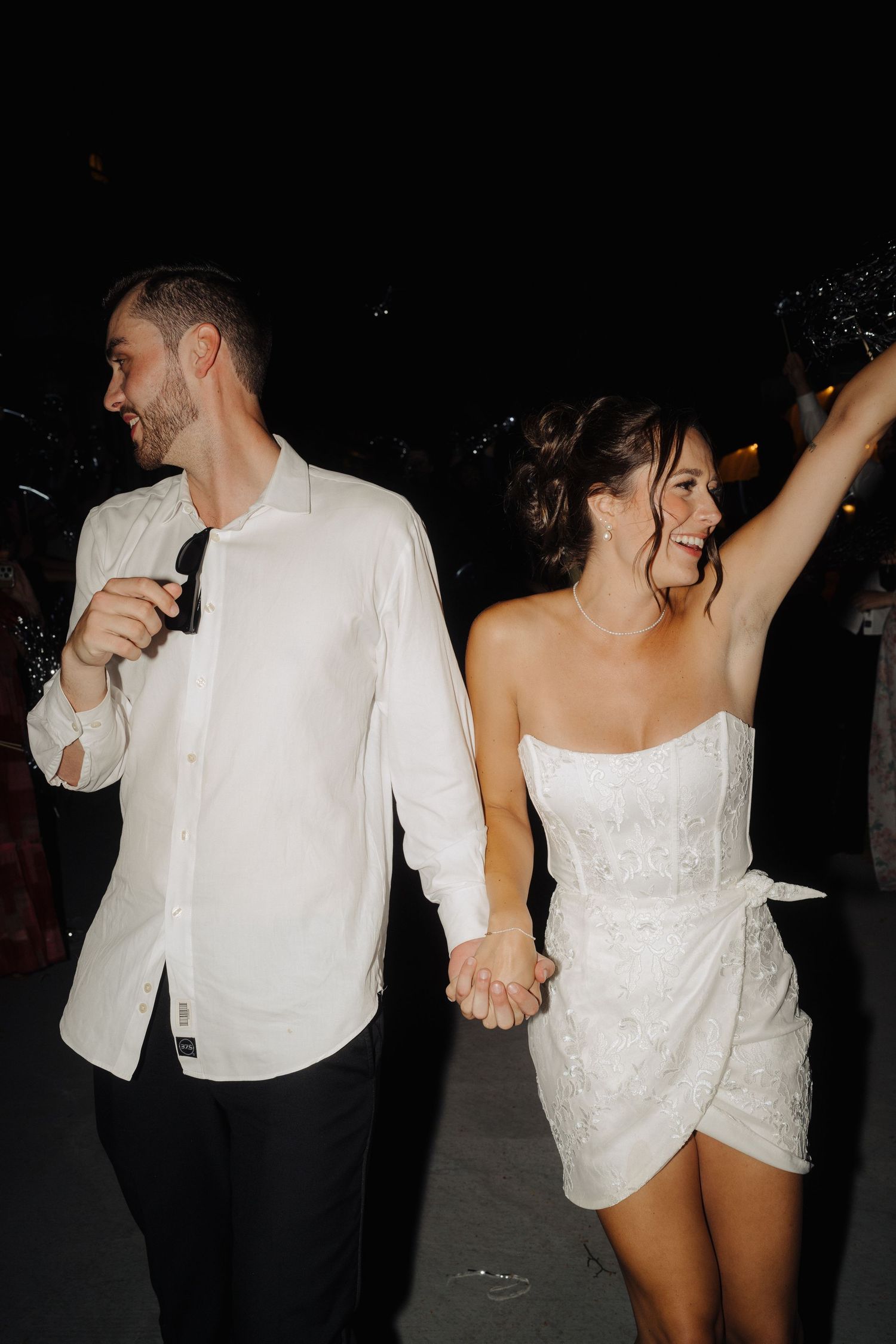 Newlyweds celebrate on the dance floor in matching white outfits during reception.